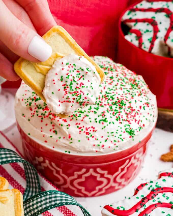 dipping a cookie into holiday cake dip with red and green sprinkles.