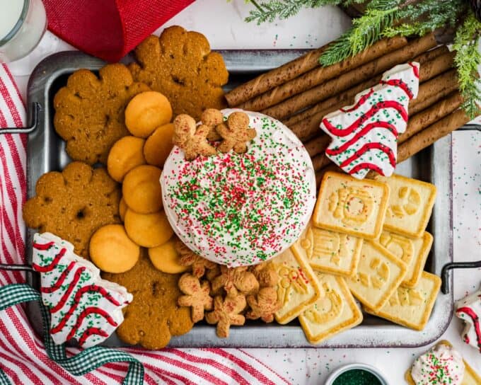 holiday platter with various cookies and a red bowl filled with christmas tree cake dip.