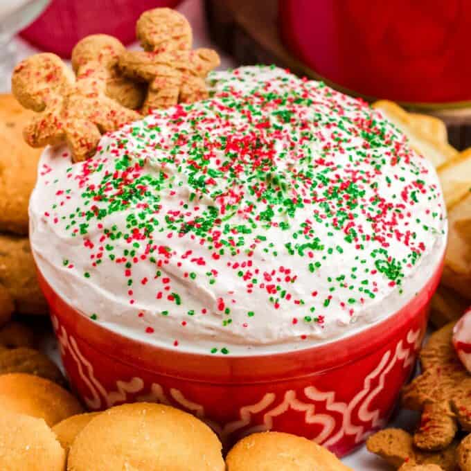 red bowl filled with christmas tree dip topped with sprinkles and surrounded by cookies.