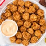 white plate full of fried pickles with a ramekin of dipping sauce