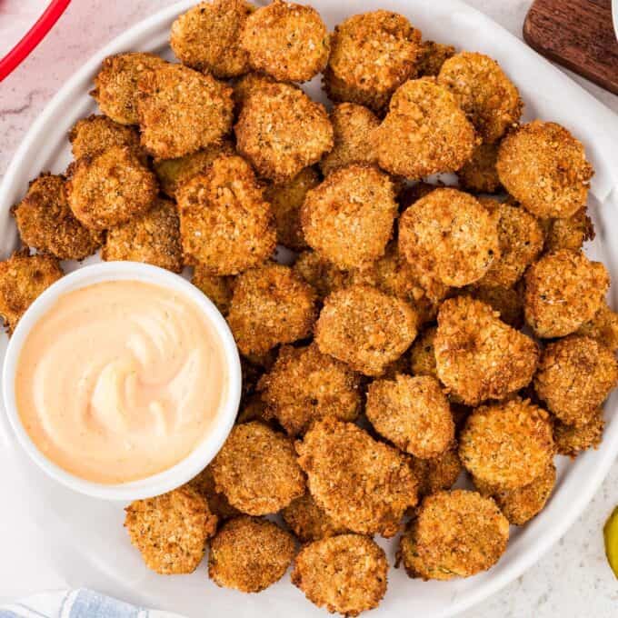 white plate full of fried pickles with a ramekin of dipping sauce