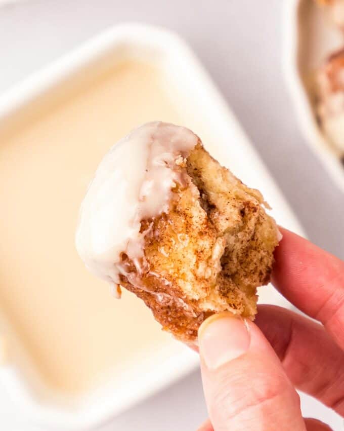 holding a cinnamon sugar monkey bread bite that's been dipped in glaze.