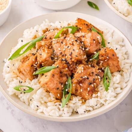 white bowl filled with white rice and ginger sesame salmon bites garnished with green onions.