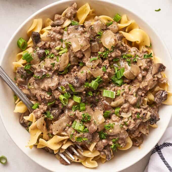 white bowl of egg noodles topped with ground beef stroganoff.