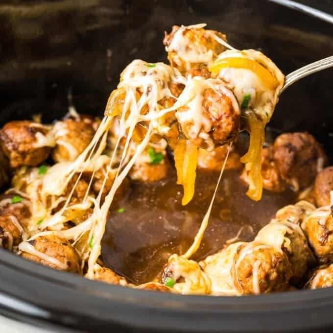 scooping a serving of meatballs in a french onion sauce with melted cheese.