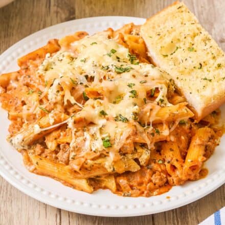 plate with a generous serving of baked penne and a slice of garlic bread.