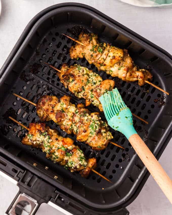 brushing chicken skewers in an air fryer with garlic parmesan butter.