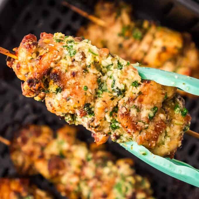 tongs holding a garlic parmesan chicken skewer.