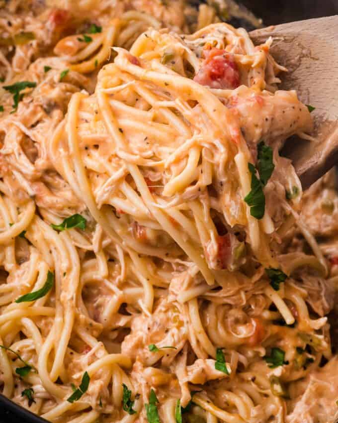 scooping some chicken spaghetti out of a slow cooker with a wooden spoon.