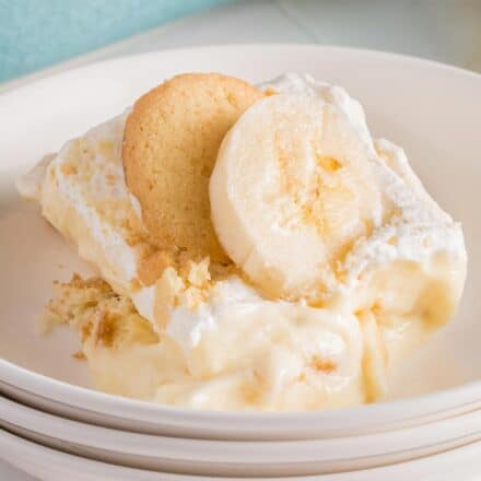serving of banana pudding on a white plate with a vanilla wafer and slice of banana.