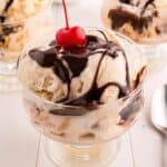 hot fudge sauce drizzled over a sundae bowl of ice cream with a cherry on top.