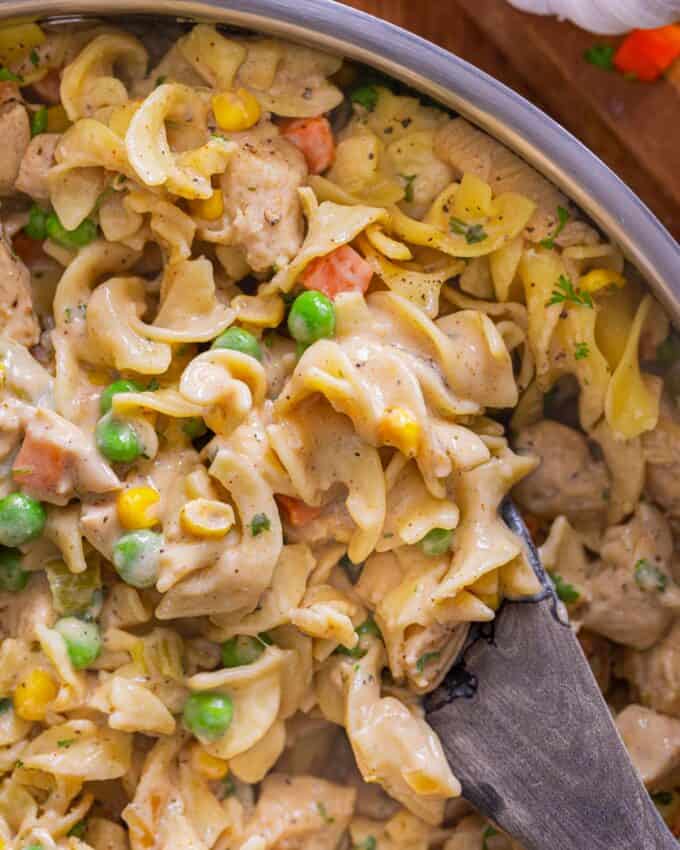 spoon stirring chicken pot pie pasta in a stainless steel skillet