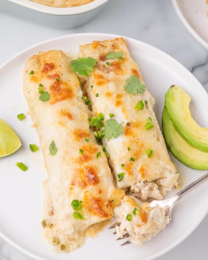 two white chicken enchiladas on a plate with avocado