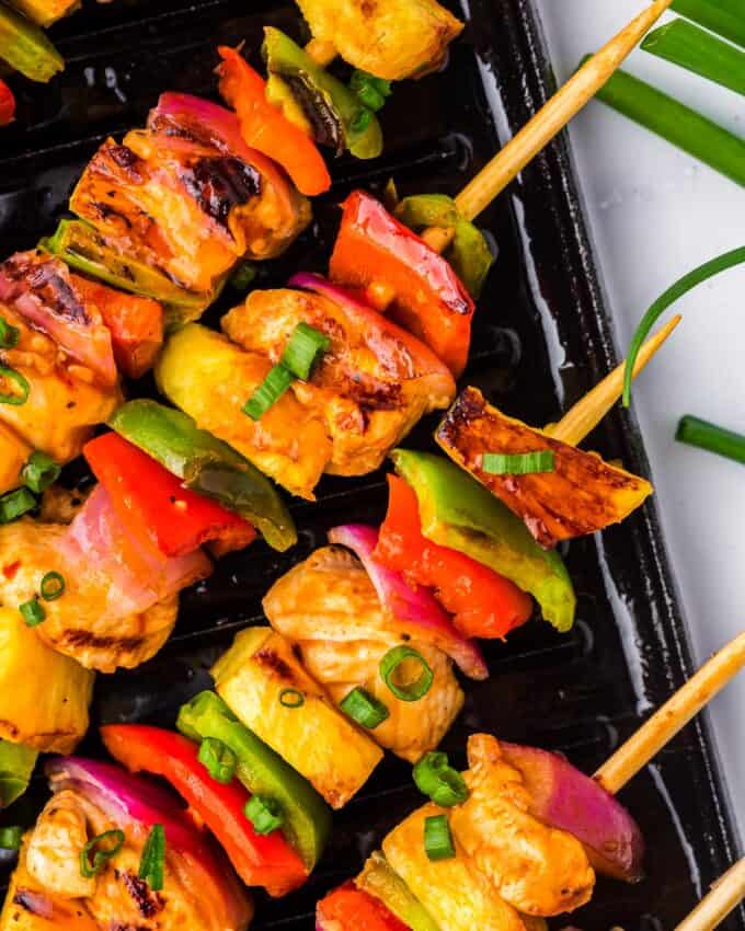 close up of chicken skewers with peppers and pineapple on a grill pan