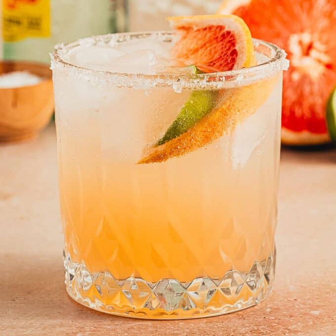 paloma cocktail in a rocks glass, garnished with a salted rim, lime slice, and grapefruit slice.