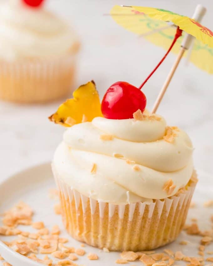 plate with a pina colada cupcake garnished with pineapple, a cherry, and a paper umbrella