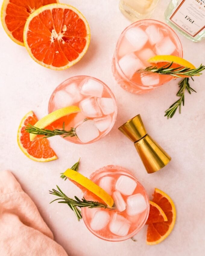 three gin fizz cocktails on a table with grapefruit and rosemary