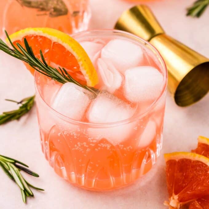 glasses filled with grapefruit gin fizz garnished with fruit and a rosemary sprig