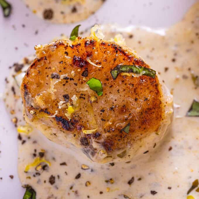 closeup photo of a seared scallop in a pesto cream sauce.