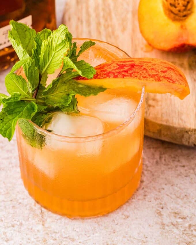 old fashioned glass with a peach bourbon smash.