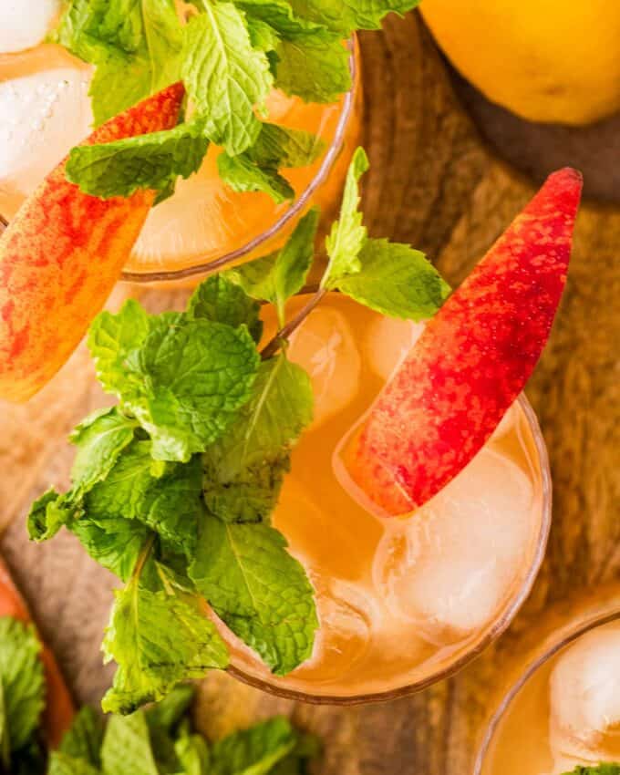 glasses of peach bourbon cocktails on a wooden board.