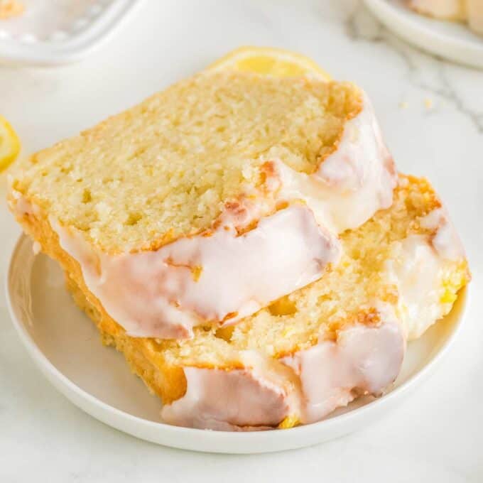 two slices of lemon loaf stacked offset on a white plate.