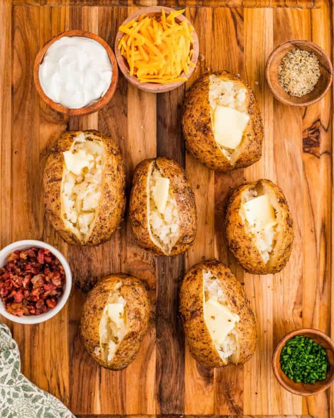 wooden board full of smoked baked potatoes and various toppings.