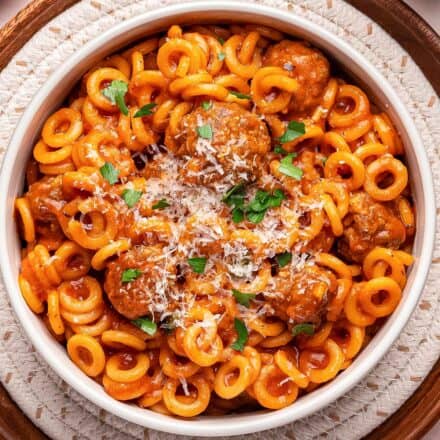 bowl of spaghettios with meatballs topped with parmesan cheese and parsley.