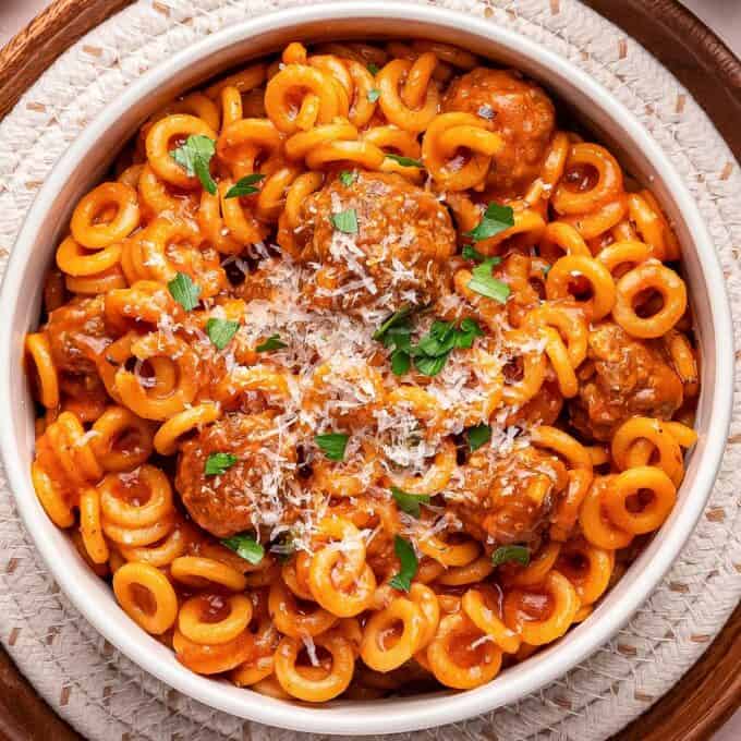 bowl of spaghettios with meatballs topped with parmesan cheese and parsley.