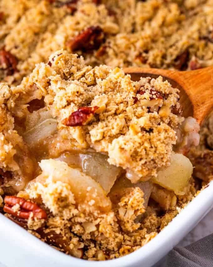 scooping pear crisp out of the baking dish with a wooden spoon