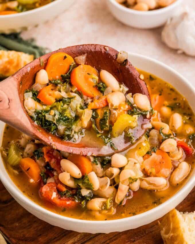 ladling tuscan bean soup into a white bowl.