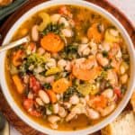 overhead view of a white bowl of tuscan white bean soup with a spoon in it