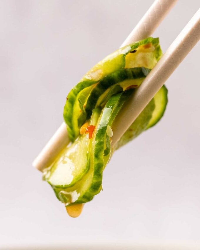pair of chopsticks holding a bite of asian cucumber salad