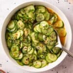 overhead photo of cucumber salad in a white bowl with a serving spoon
