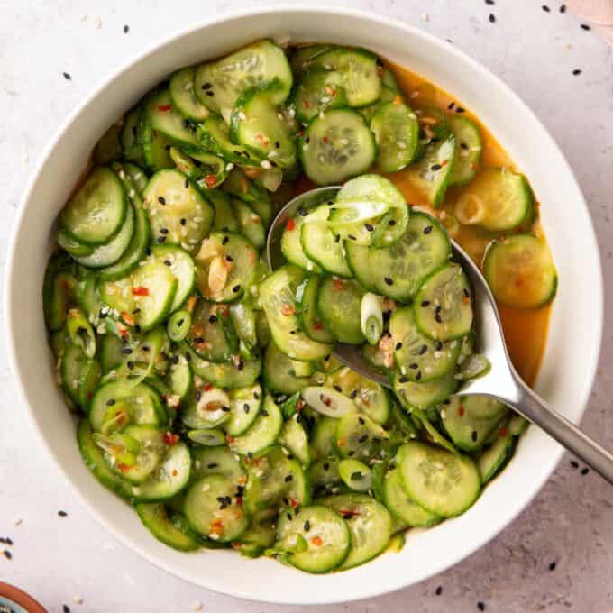 overhead photo of cucumber salad in a white bowl with a serving spoon
