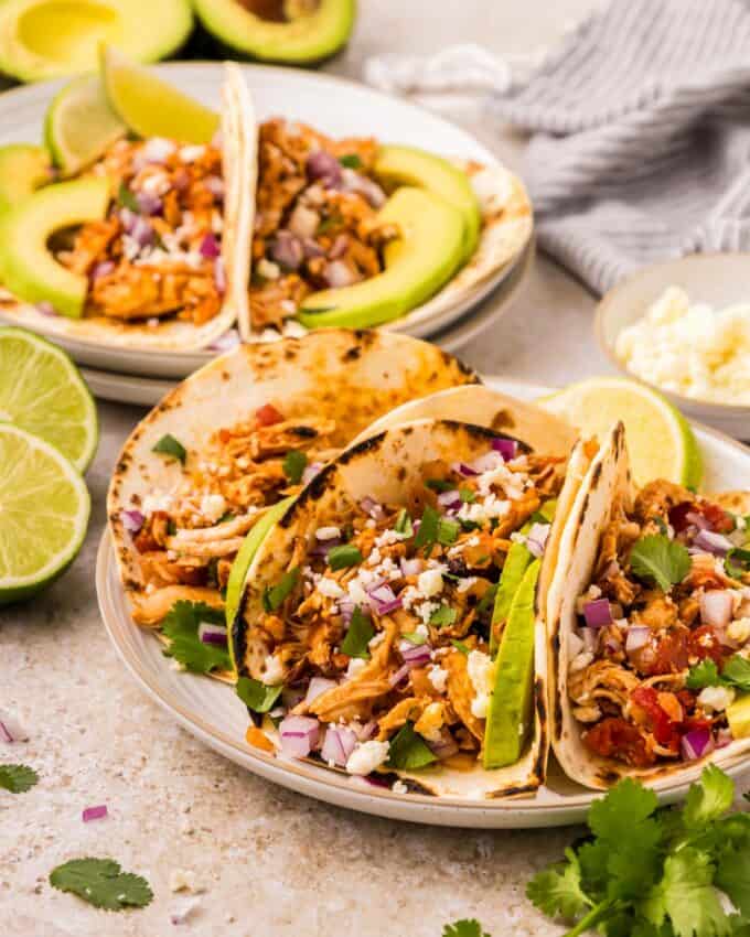 two plates of chicken tinga tacos with all the toppings