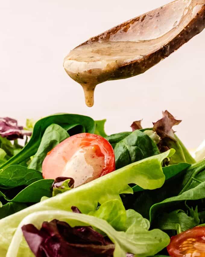 wooden spoon pouring italian dressing onto a green salad