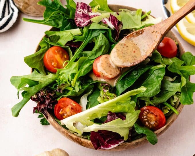 spooning italian dressing over a green salad with tomatoes