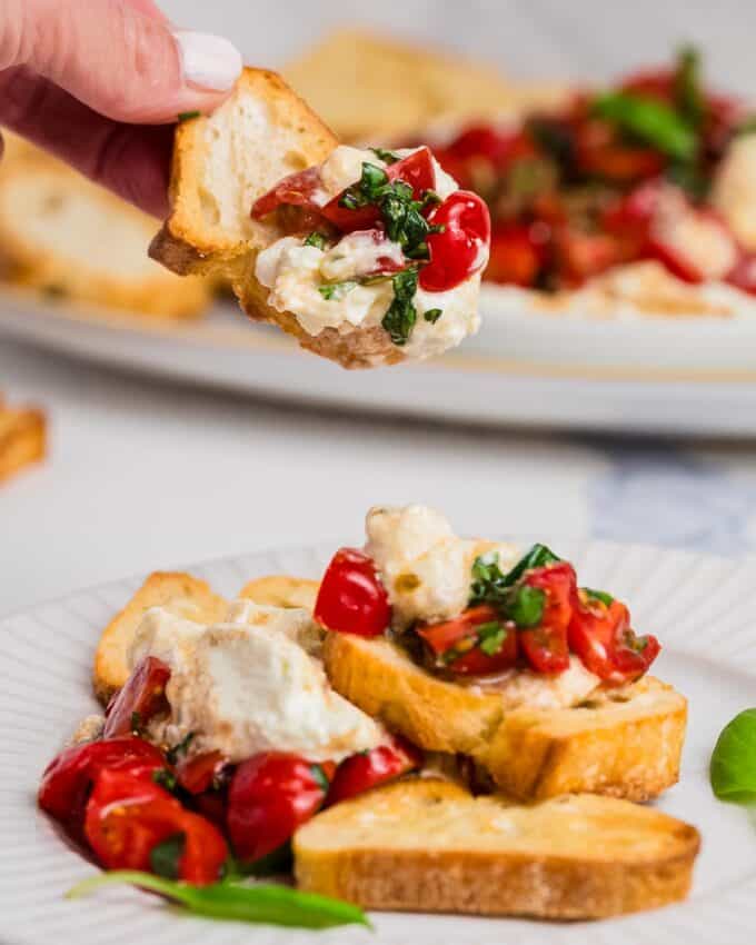 hand holding whipped feta and bruschetta dip on a crusty piece of bread