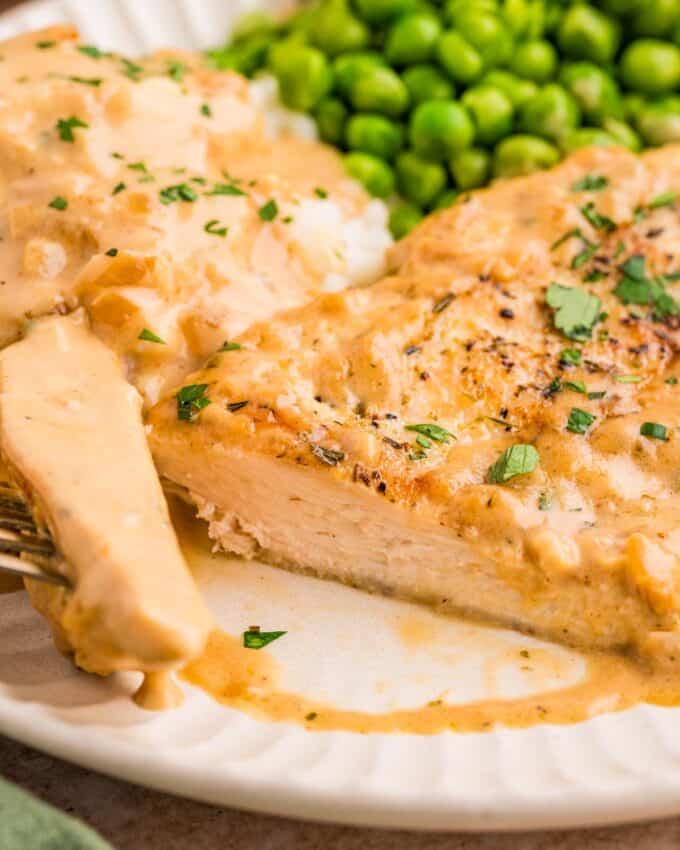 dijon chicken sliced on a plate with mashed potatoes and peas