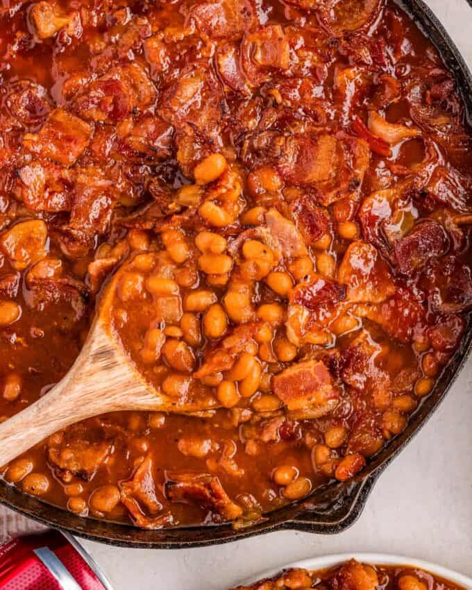 wooden spoon scooping into a skillet of baked beans